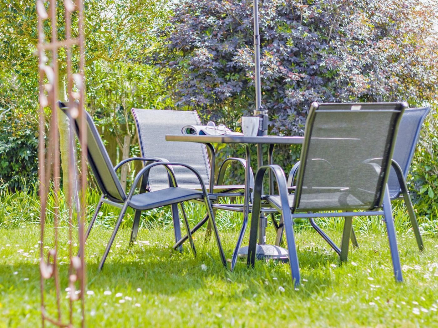 Un espace aménagé en jardin, avec une table et quatre chaises, entouré de verdure et délimité par une clôture en métal.