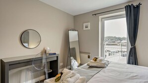 A hotel room with a bed, a mirror, a bedside table with a lamp, a window with curtains, and a view of the outside. - 1 Bed in Oban (oc-96079) (Oban)