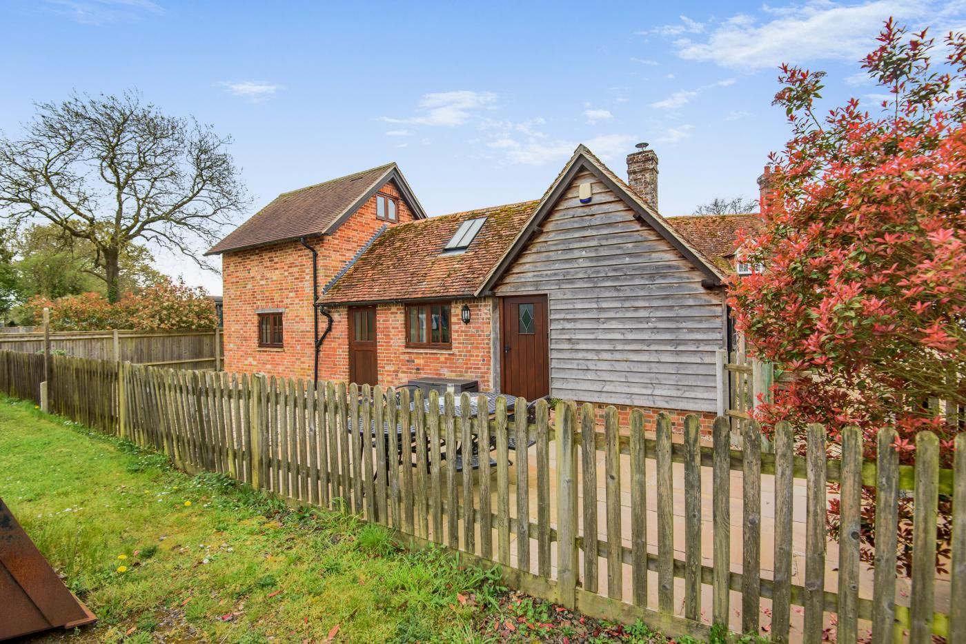 A two-story house with a brick exterior and a wooden extension, surrounded by a wooden fence.