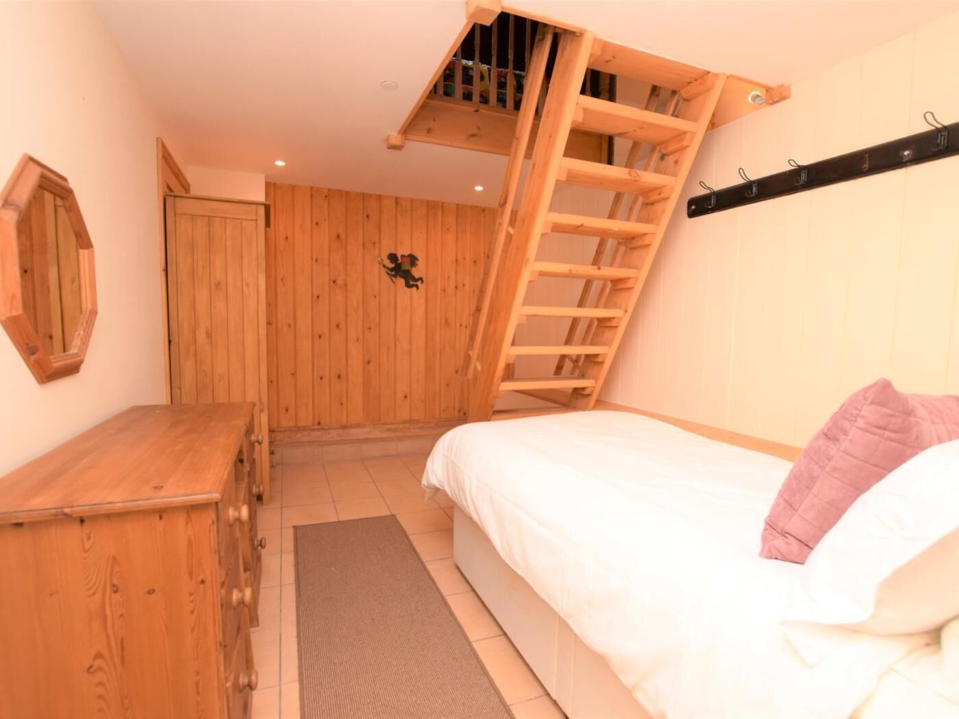 Een slaapkamer met een houten ladder, een bed met wit beddengoed, een dressoir en een spiegel aan de muur.