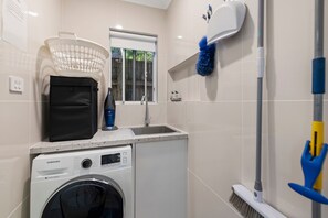 A compact laundry area with a washing machine, a drying rack, a window, and a broom.