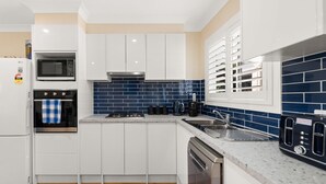 Cozinha moderna com armários brancos, painel de azulejos azuis, eletrodomésticos de aço inoxidável e uma janela com persianas.