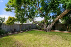 A backyard with a large tree, a wooden fence, and a grassy lawn.