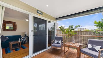 A covered outdoor deck with a sliding glass door leading to a living room, furnished with a sofa, a coffee table, and two chairs.