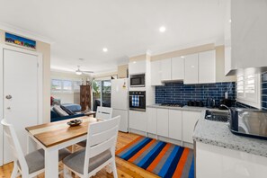 A modern kitchen with white cabinets, a microwave, oven, and a gas stove. There is a dining area with a wooden table and chairs.