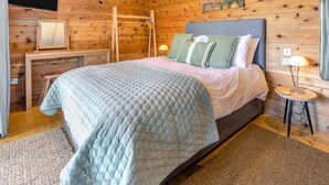 A wooden-paneled room with a bed, a desk, a hanging rack, and a painting on the wall. - 3 Bed in Cullompton (oc-96118) (Willand)