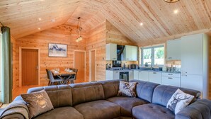 A modern log cabin interior with a sectional sofa, a dining area, and a kitchen. - 3 Bed in Cullompton (oc-96118) (Willand)