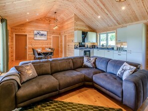 A modern log cabin interior with a sectional sofa, a dining area, and a kitchen. - 3 Bed in Cullompton (oc-96118) (Willand)