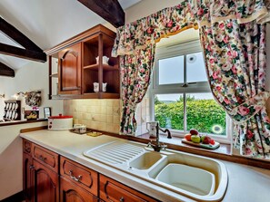 Eine Küche mit Holzausstattung, einem Spülbecken und einem Fenster mit floralem Vorhang.