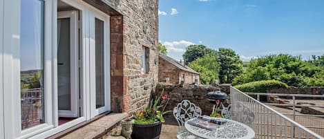 A stone building with a balcony, outdoor seating, and a view of the countryside.