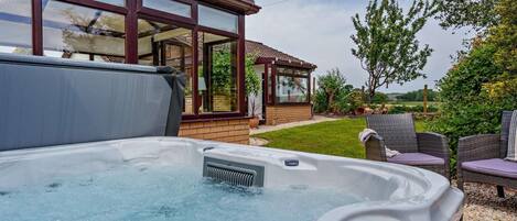 Ein Whirlpool mit Bedienfeld, eine Holzterrasse und ein Haus mit großen Fenstern.
