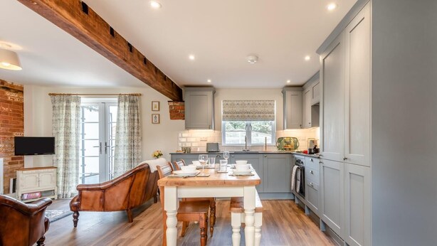 A modern kitchen with wooden flooring, a dining area with a wooden table and chairs, and grey cabinets. - 2 Bed in Fordingbridge (oc-96125) (Godshill)