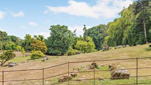 A landscaped garden with a metal fence, trees, and rocks. - 2 Bed in Fordingbridge (oc-96125) (Godshill)