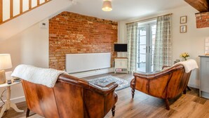 A cozy living room with a brick wall, a fireplace, a television, and a dining area with a kitchen counter. - 2 Bed in Fordingbridge (oc-96125) (Godshill)