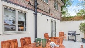 A wooden dining table with chairs, a grill, and a potted plant in a backyard. - 3 Bed in Fordingbridge (oc-96126) (Godshill)