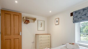 A bedroom with a wooden door, a dresser, a mirror, and two beds with towels. - 3 Bed in Fordingbridge (oc-96126) (Godshill)