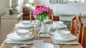 A dining table set with white plates, bowls, and cutlery, a vase with pink flowers, and a glass of water. - 3 Bed in Fordingbridge (oc-96126) (Godshill)
