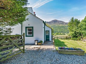 A white house with a green door and window, a gravel driveway, a wooden gate, and a mountain in the background. - 1 Bed in Cockermouth (oc-96138) (Buttermere)