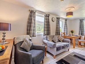 A living room with a sofa, armchair, dining table, and a lamp. - 1 Bed in Cockermouth (oc-96138) (Buttermere)