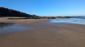 Een strand met heldere lucht, rotsformaties en een zandstrand.