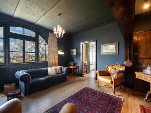 A room with a dark blue sofa, a wooden chair, a patterned rug, and a chandelier.