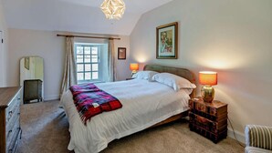 A bedroom with a large bed, two bedside lamps, a window with curtains, a mirror, and a framed picture on the wall.