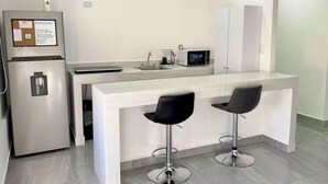 A modern kitchen with a refrigerator, microwave, sink, and two bar stools. - Studio apartment on 5th Avenue, just steps from the beach, the ferry, ADO buses, parks, and more (Playa del Carmen)