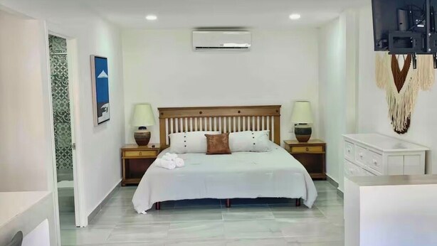 A bedroom with a bed, bedside lamps, a TV, and a white dresser. - Studio apartment on 5th Avenue, just steps from the beach, the ferry, ADO buses, parks, and more (Playa del Carmen)