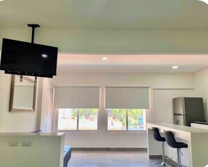 A modern kitchen with a flat-screen TV, large windows, and a bar area. - Studio apartment on 5th Avenue, just steps from the beach, the ferry, ADO buses, parks, and more (Playa del Carmen)