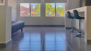 A modern room with a large window, a blue sofa, and two bar stools. - Studio apartment on 5th Avenue, just steps from the beach, the ferry, ADO buses, parks, and more (Playa del Carmen)
