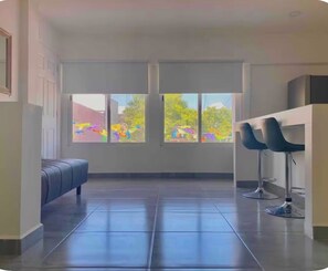 A modern room with a large window, a blue sofa, and two bar stools. - Studio apartment on 5th Avenue, just steps from the beach, the ferry, ADO buses, parks, and more (Playa del Carmen)