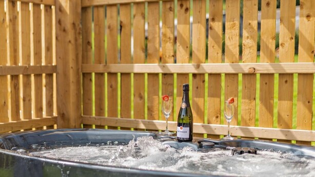 Ett bubbelbad med en flaska och glas, omgivet av ett trästaket.