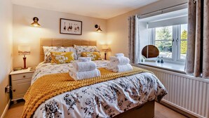 Un dormitorio con cama, lámparas de noche, una ventana con cortinas y un cuadro en la pared.