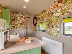 A kitchen with floral wallpaper, a wooden counter, a loaf of bread, and a bottle of mustard.