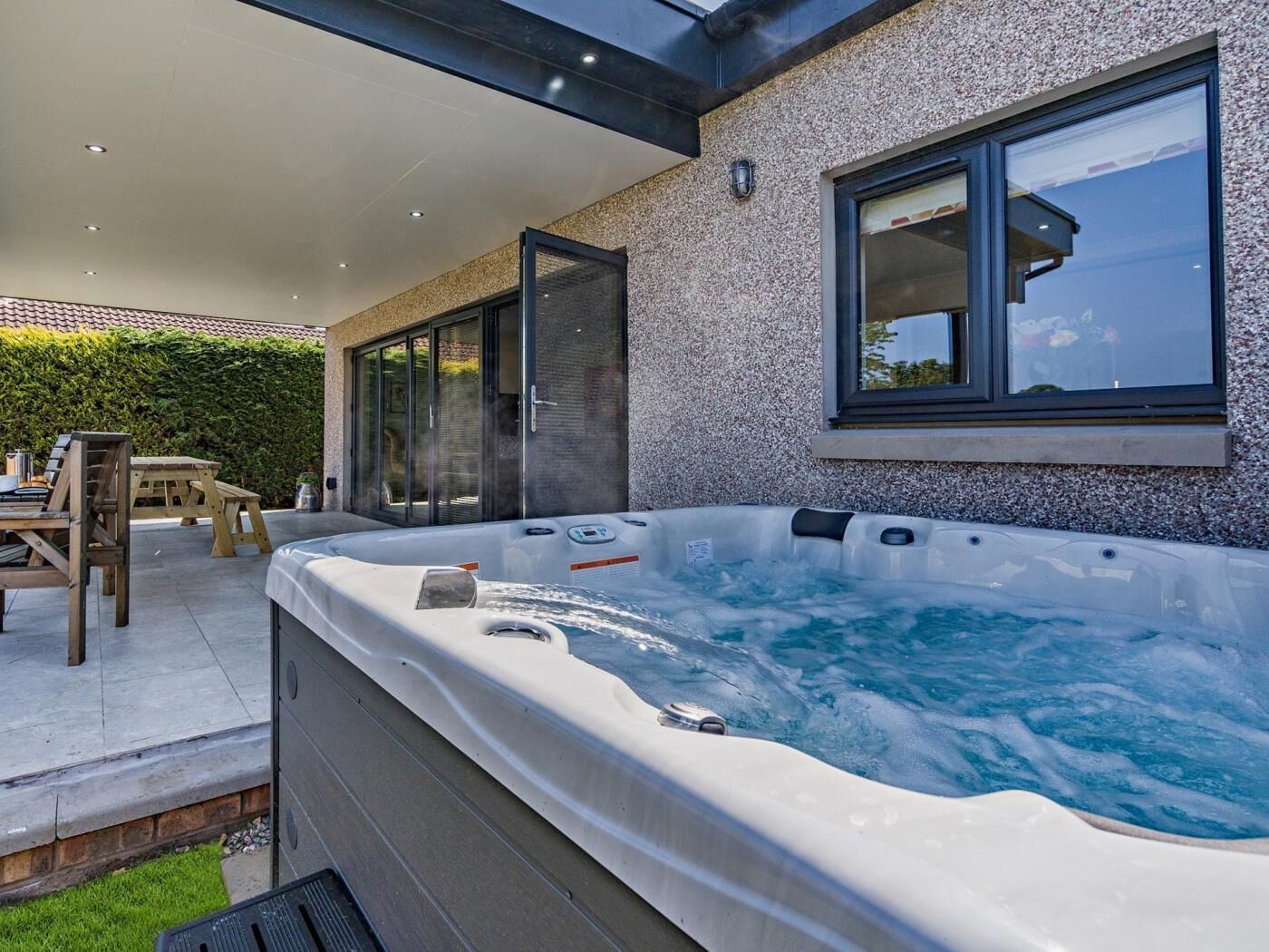 Un jacuzzi con cerramiento de vidrio, una mesa de patio y una silla.