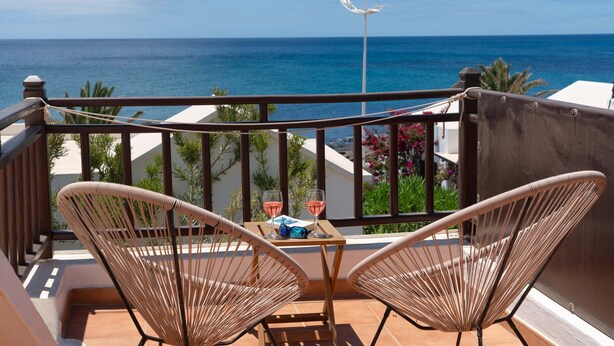 Un balcone con sedie in vimini, un tavolo e due bicchieri di vino rosa.