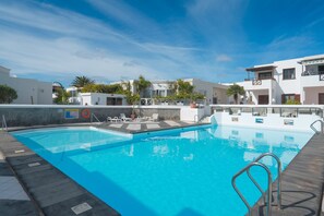 Ein Pool mit Holzboden, umgeben von weißen Gebäuden mit Balkonen und Palmen.