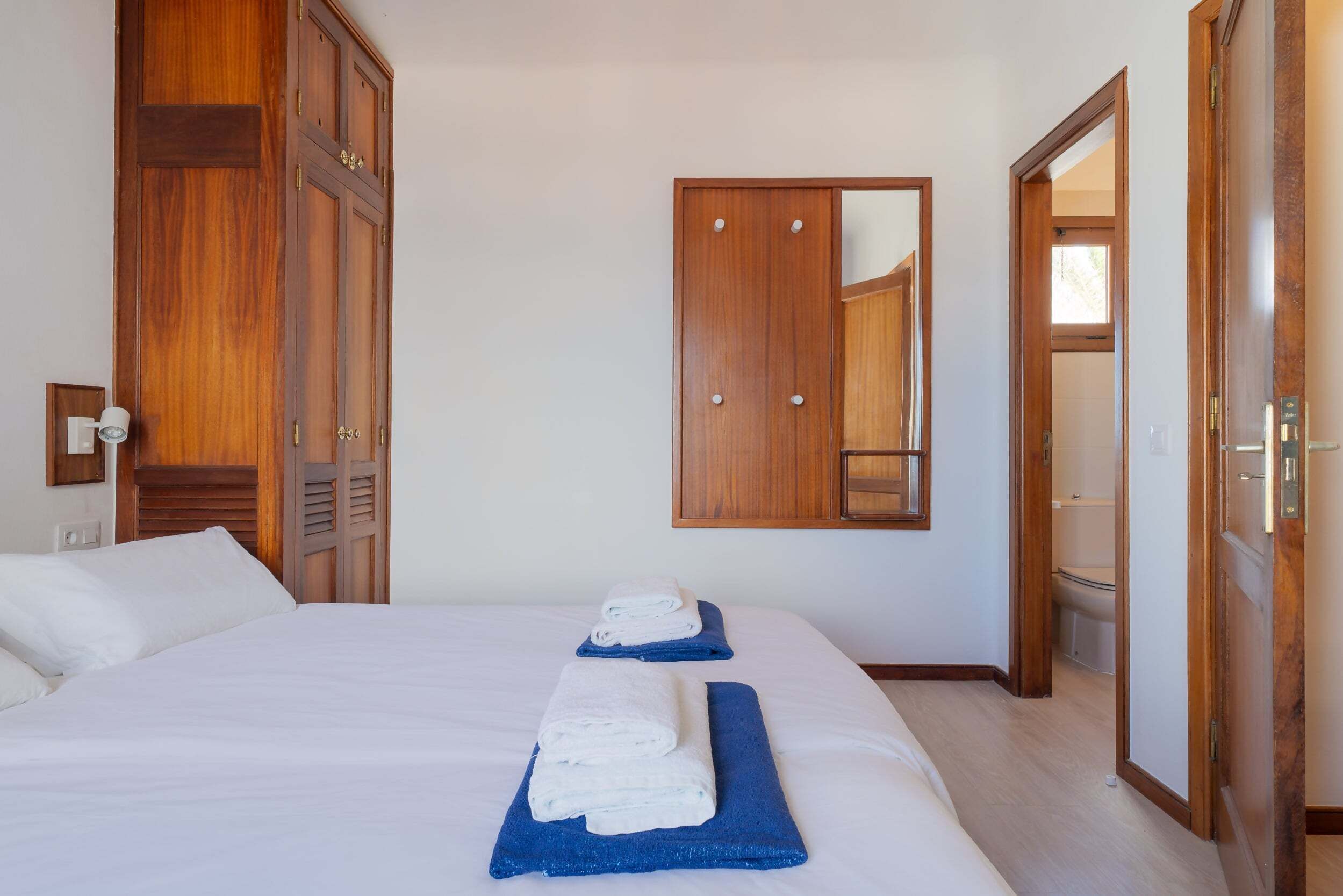 A hotel room with a large bed, wooden wardrobe, and a mirror.