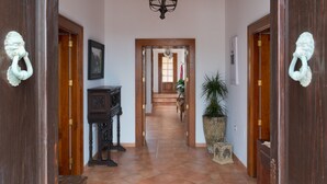Un pasillo con puertas de madera, un candelabro, un cuadro enmarco, una planta en maceta y un aparador de madera.