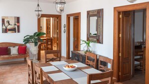 Comedor con mesa de madera, sillas, un cuenco de fruta y una planta en maceta.