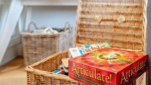 Een rieten mand met een doosje met de tekst 'Articulate! The Fast Talking Description Game' op een houten vloer.