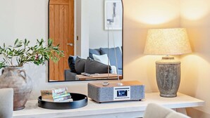 Een kamer met een witte console tafel, een grijze speaker, een lamp, een spiegel en een plant.