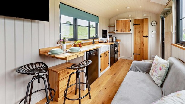 Een compacte keuken met houten kastjes, een inbouwvaatwasser en een raam met uitzicht op een groen landschap.