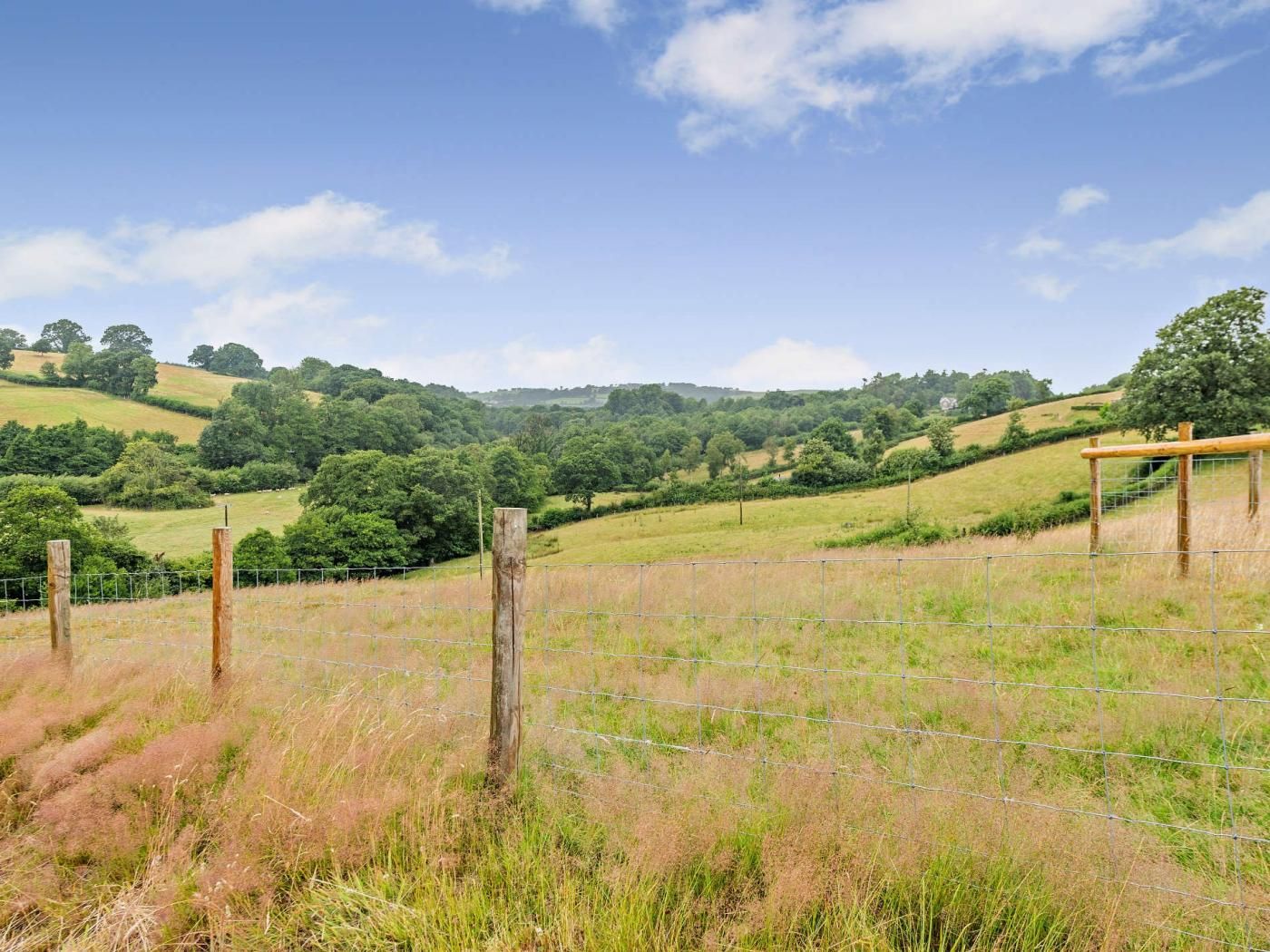A rural landscape with a fenced field, wooden posts, and a hill in the background.