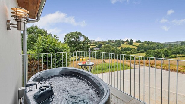 A hot tub on a balcony with a view of rolling hills and a table with drinks. - 1 Bed in South Molton (oc-96105) (South Molton)