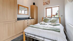 A bedroom with a bed, wooden wardrobe, a mirror, a window with a view, and a wall-mounted light fixture. - 1 Bed in South Molton (oc-96105) (South Molton)