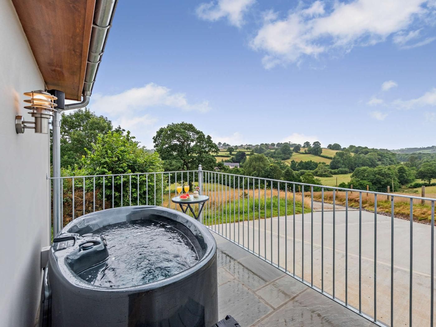 A balcony with a hot tub, a table with drinks, and a view of rolling hills.