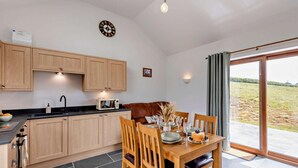 A kitchen with wooden cabinets, a dining table with chairs, a microwave, and a view through a glass door. - 1 Bed in South Molton (oc-96105) (South Molton)