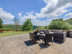 An outdoor patio with stone flooring, wicker furniture, and a view of green hills. - 3 Bed in Buxton (oc-96211) (Cressbrook)