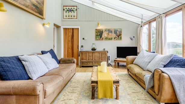 A spacious living area with a high ceiling, a wooden cabinet, a television, and a large window. - 3 Bed in Buxton (oc-96211) (Cressbrook)